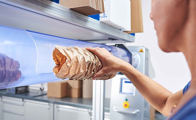 A woman removing brown paper cushioning from a machine