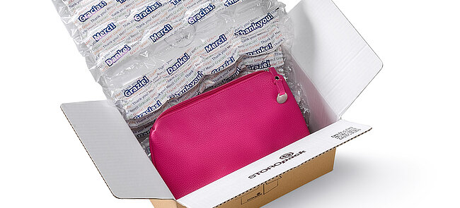 A cardboard box containing a pink bag and air cushions with a printed design