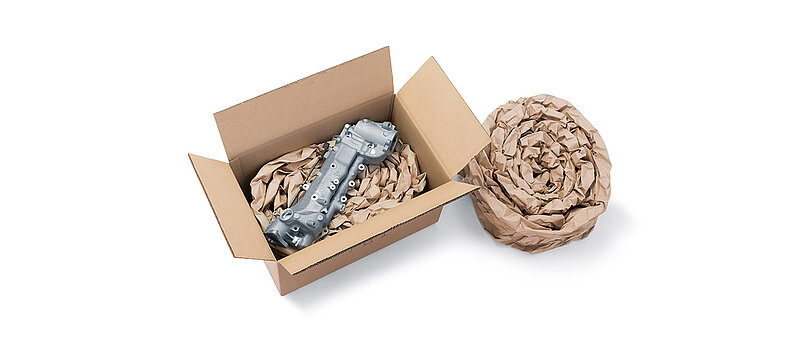 A cardboard box containing a component and paper cushioning made from rolled-up paper cushioning strips