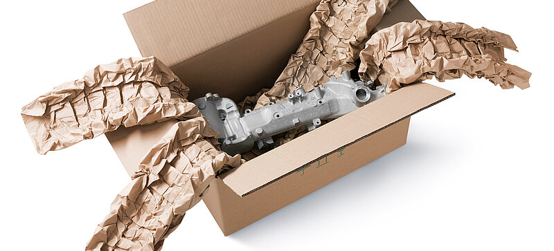 A cardboard box containing an engine component and brown paper cushioning